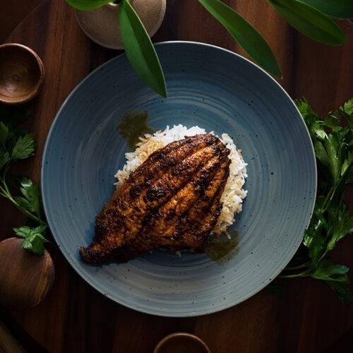 A blackened catfish filet sitting on a bed of rice.