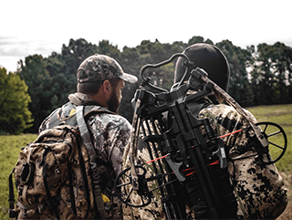 Two people in camo take their crossbow into the woods