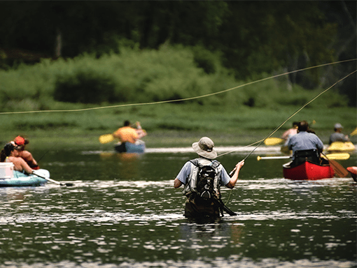 A fisherman casts in a river crowded with canoes