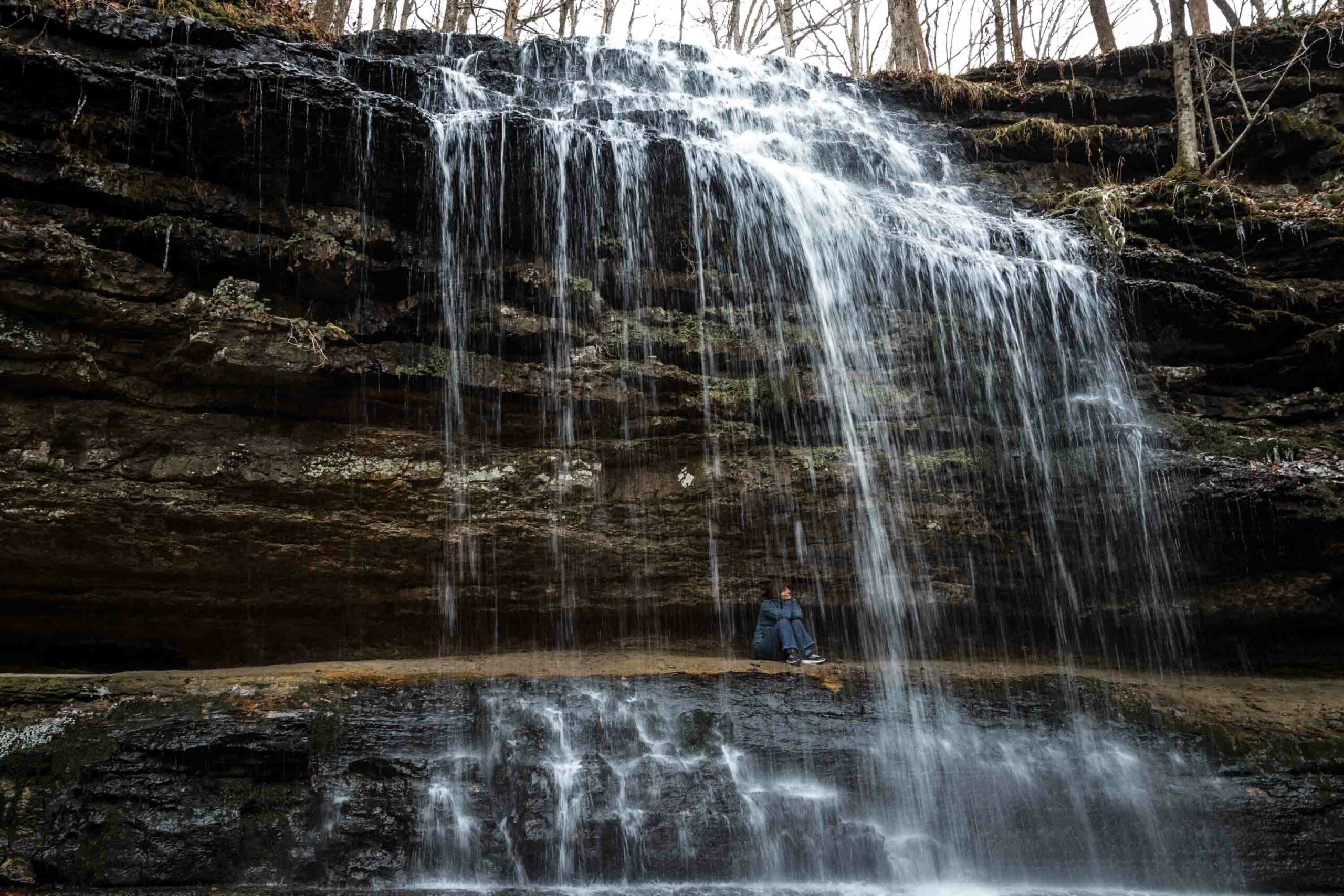 Person sitting under a waterfall