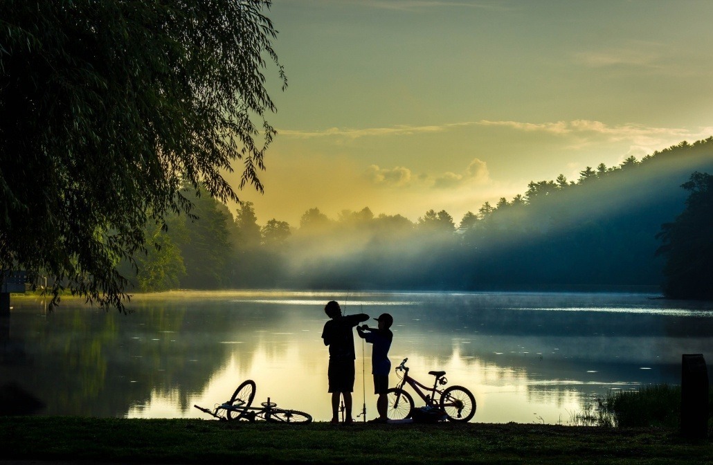 Two children with fishing poles by the lake at dusk.