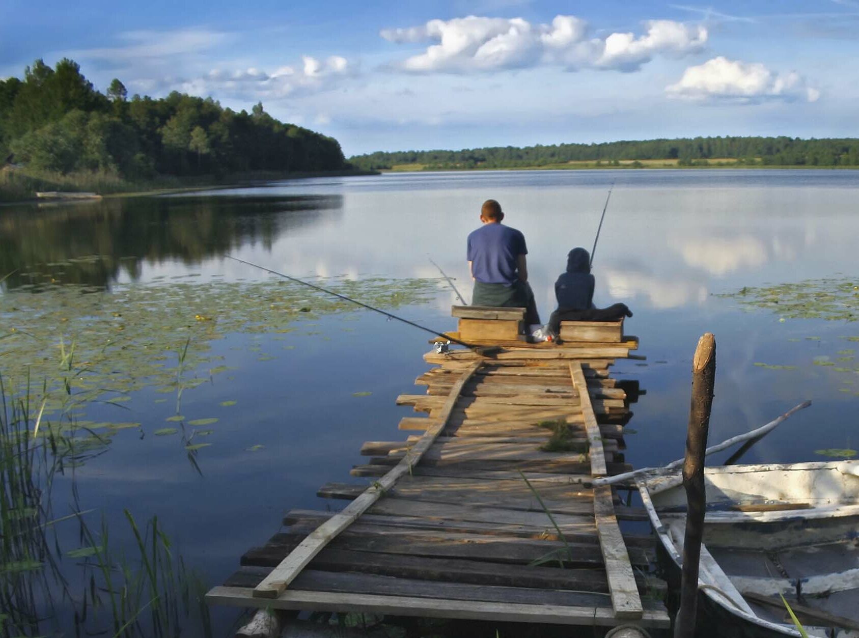 Two people fishing at the end of an old dock
