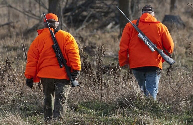 Hunters in blaze orange jackets walking away, toward the woods