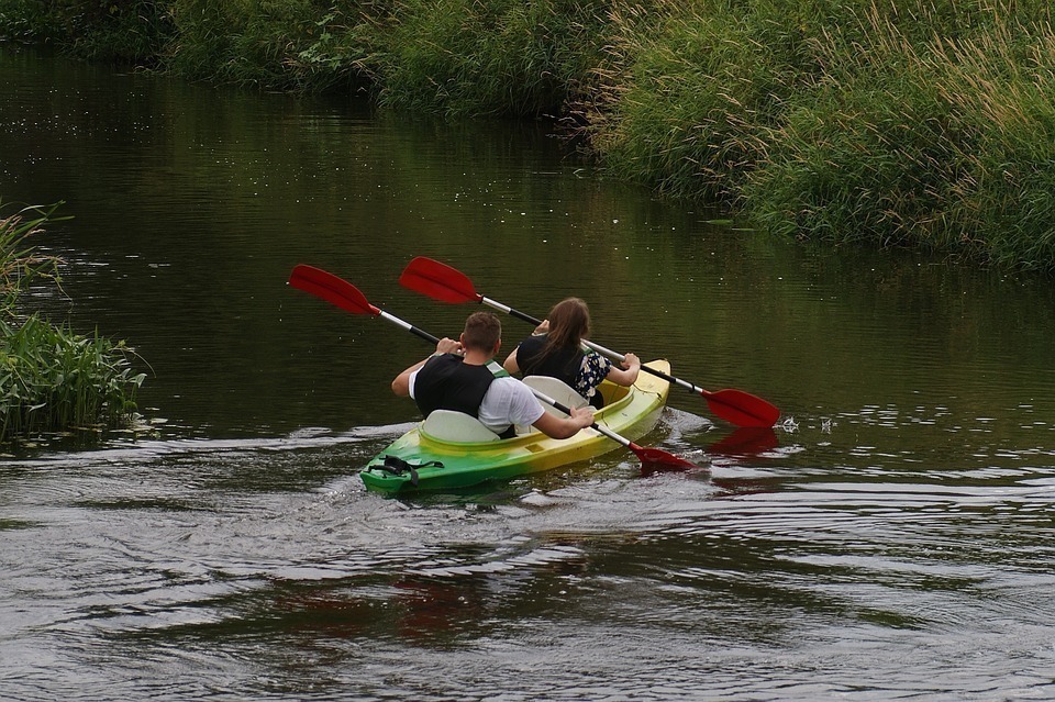 Two people in a yellow and green kayak paddling into a channel.