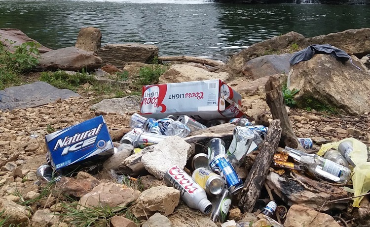 Pile of trash on rocky bank next to a body of water.