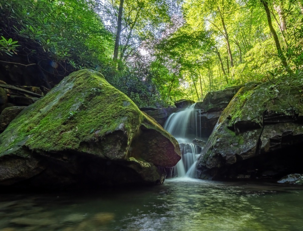 Creek waterfall among giant moss-covered rocks. 